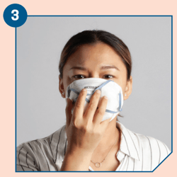 With both straps held on the top panel, place opened respirator in one hand against your face, with the nosepiece across the bridge of your nose.